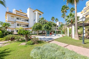 Relax in a serene courtyard surrounded by lush greenery and palm trees, featuring a playground with a slide and swings.