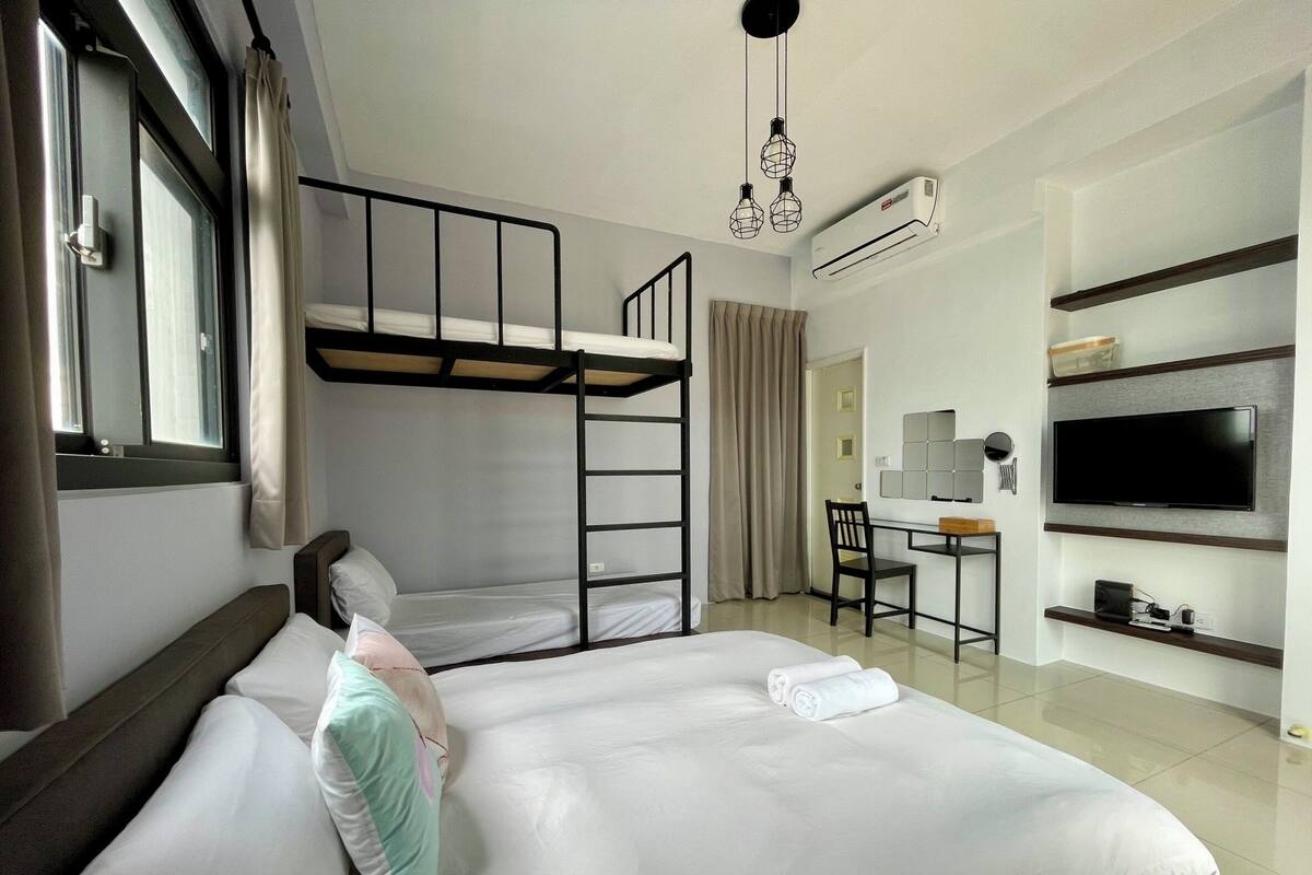 A hotel room with a bunk bed, a desk with a chair, a TV, and an air conditioning unit.