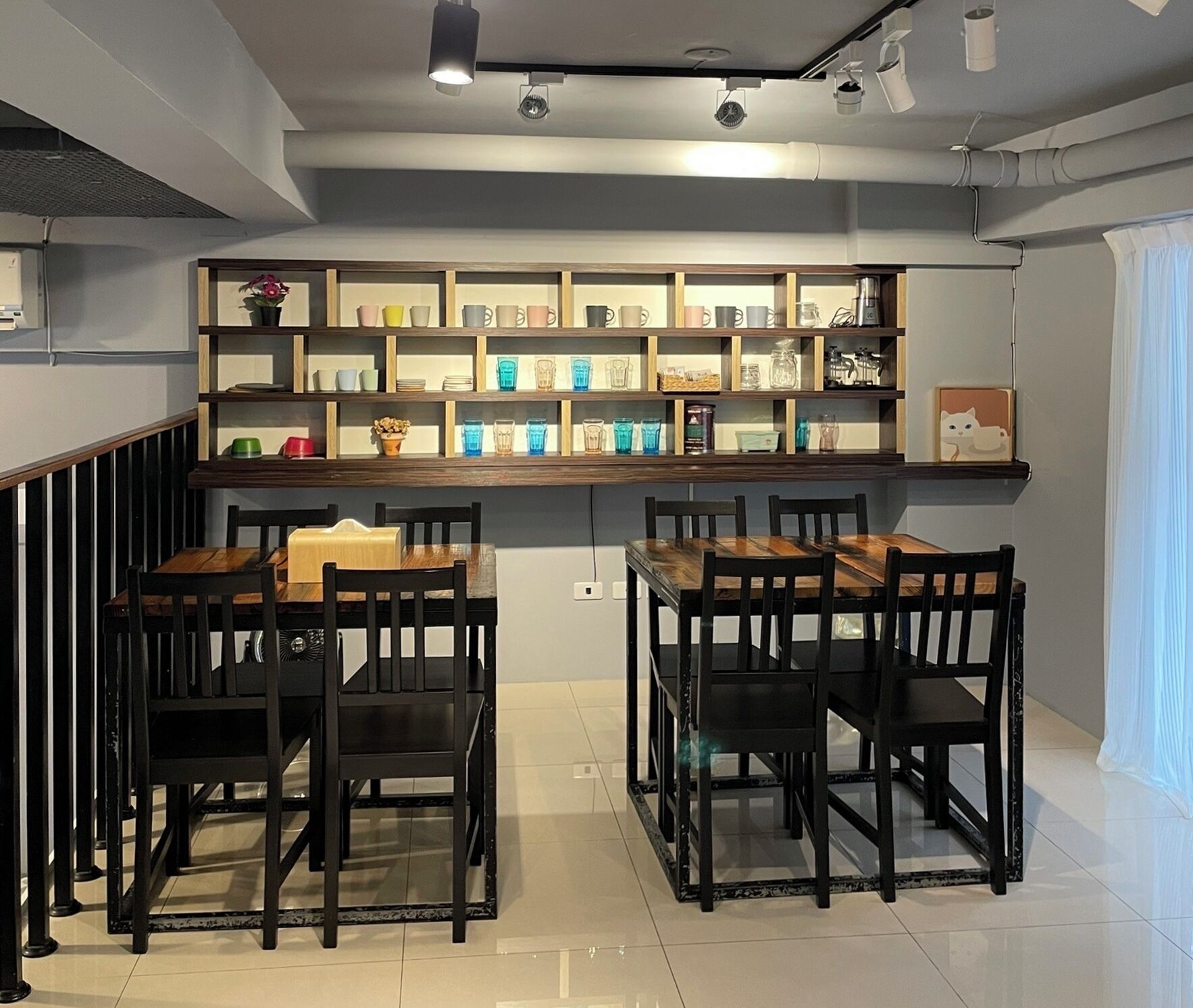 Un restaurant doté d’un long comptoir et de plusieurs tables, chacune étant accompagnée de chaises. Des étagères au-dessus du comptoir présentent divers articles.