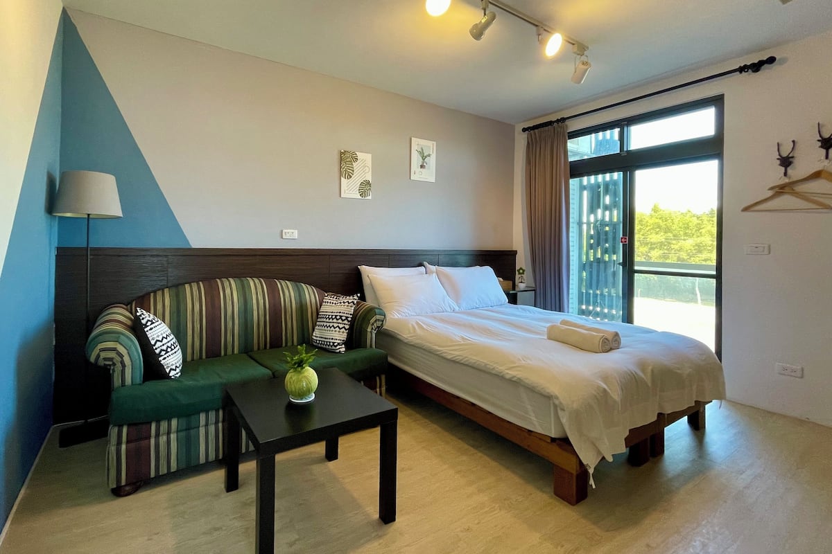 A bedroom with a bed, a sofa, a table, and a lamp.