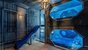 Una habitació amb tobogan, finestres hexagonals que ofereixen vistes espacials i una decoració interior inspirada en el cel estrellat.