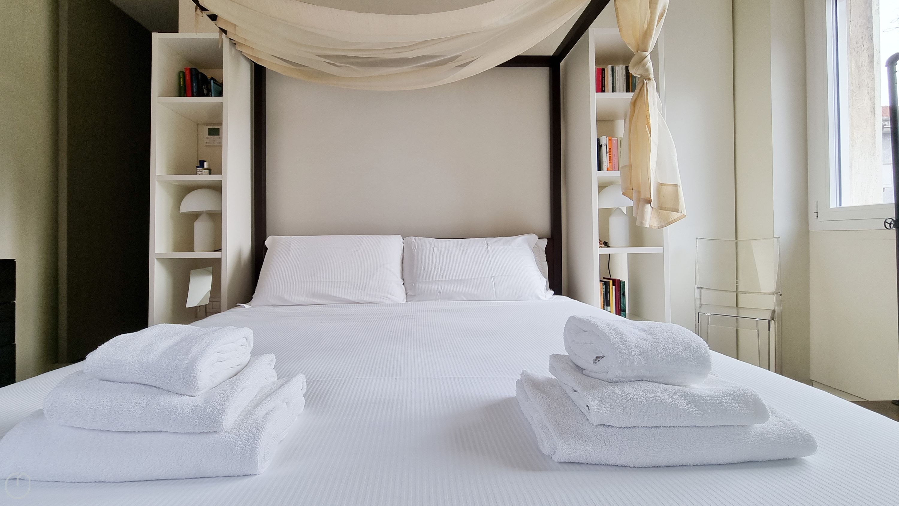 A neatly made bed with white linens and two folded towels on either side.