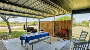 A covered patio area with a table, chairs, and a grill.