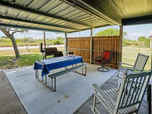 A covered patio area with a table, chairs, and a grill.