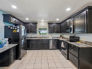A modern kitchen with dark cabinetry, stainless steel appliances, and a tiled floor. - Sorry Charlie's | Waterfront Serenity (Rockport)