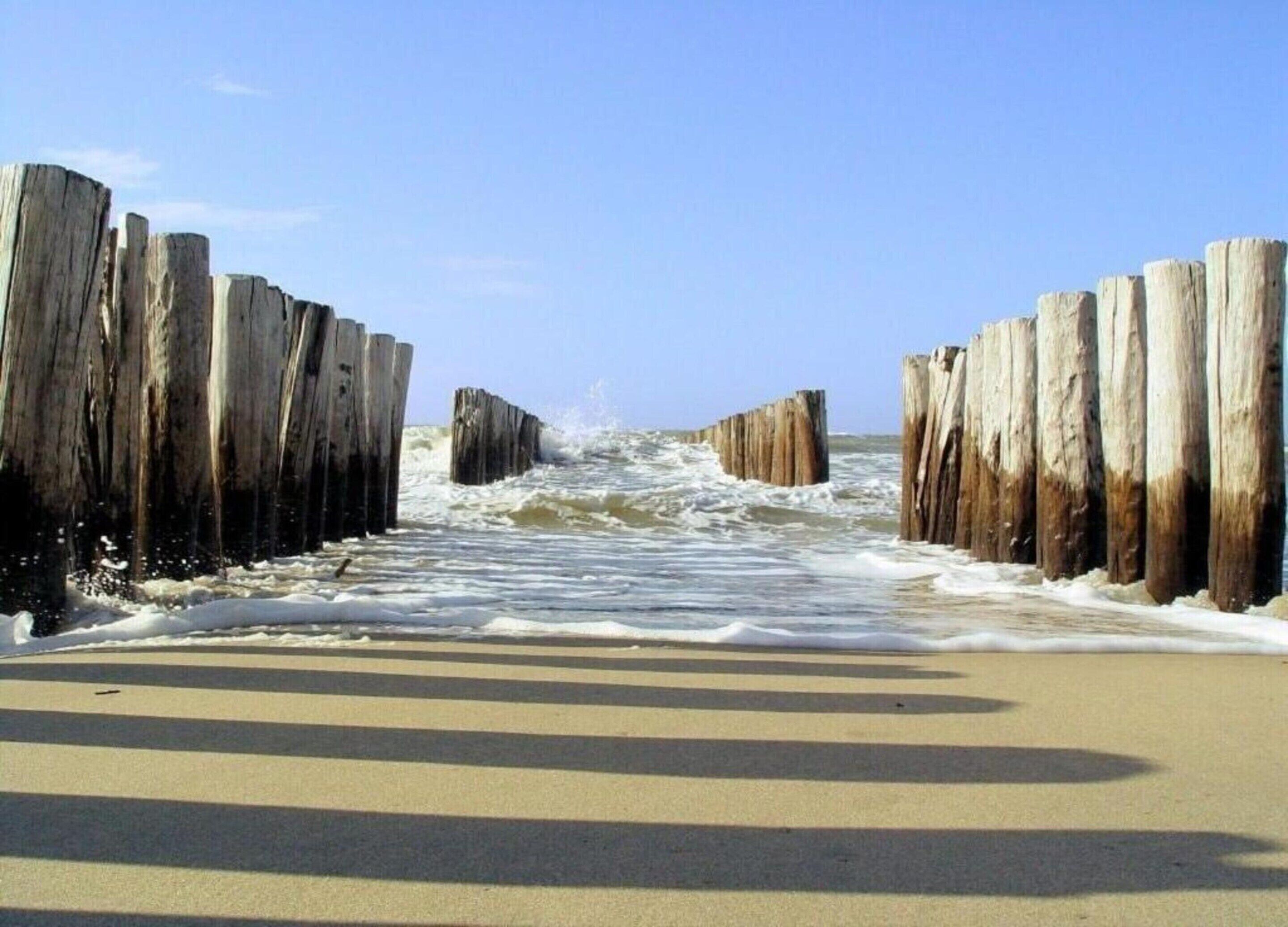 A beach with wooden groynes and waves crashing onto the shore.