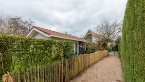 A gravel path leading to a house with a red-tiled roof, surrounded by a wooden fence and a hedge. - Holiday Home Near Beach (Oostkapelle)