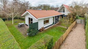 A single-story house with a red-tiled roof, a small patio with a table and chairs, and a fenced yard. - Holiday Home Near Beach (Oostkapelle)