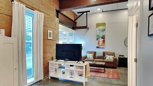 A living room with a TV, white entertainment unit, brown leather sofa, and a red rug. - Tremont Meilleur 104 | A Downtown Escape (Galveston)