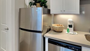 A stainless steel refrigerator and dishwasher in a kitchen with white cabinets, a woven basket, and a dish soap dispenser. - Tremont Meilleur 104 | A Downtown Escape (Galveston)