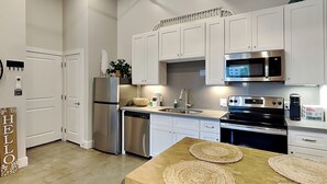 A modern kitchen with stainless steel appliances, white cabinetry, and a wooden island with woven placemats. - Tremont Meilleur 104 | A Downtown Escape (Galveston)