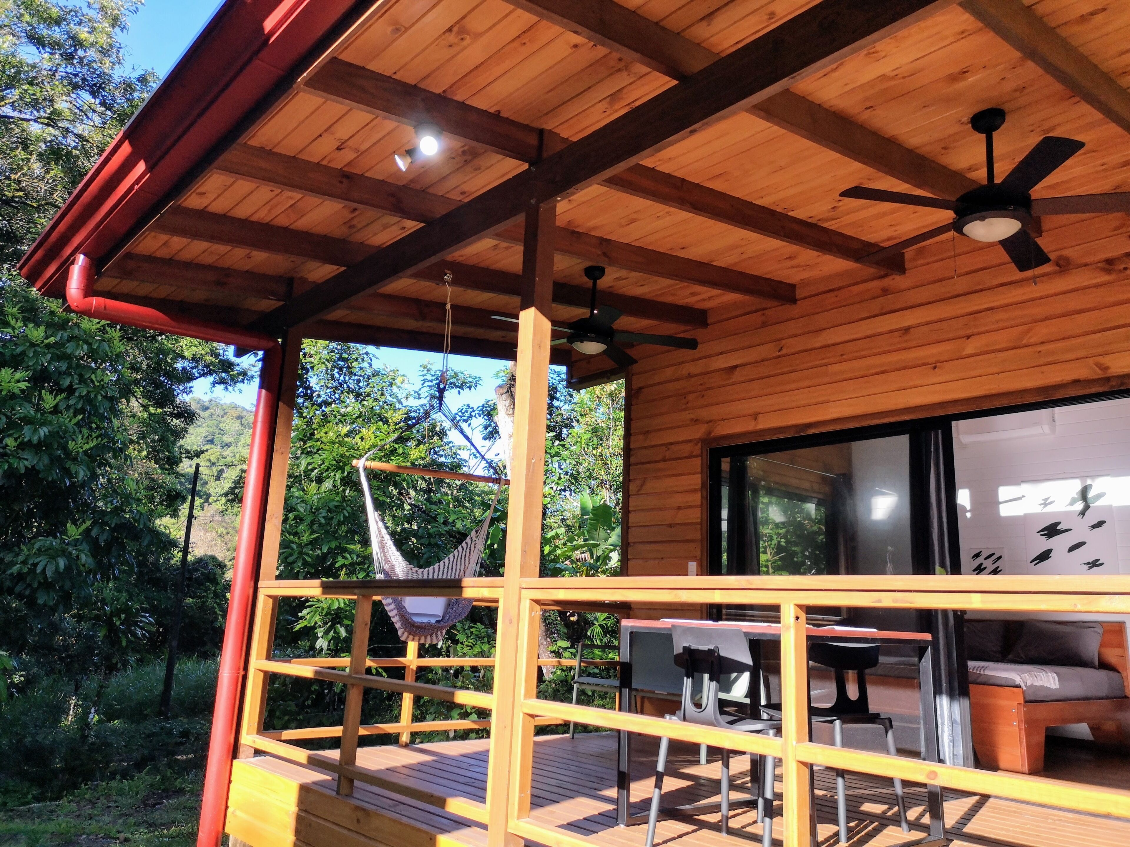 A wooden deck with a hammock, a table, chairs, and a ceiling fan.