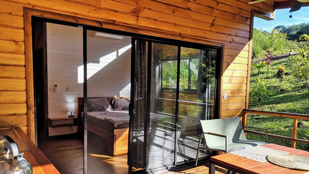 Een houten chalet met een schuifdeur naar een balkon met uitzicht op een weelderige tuin.
