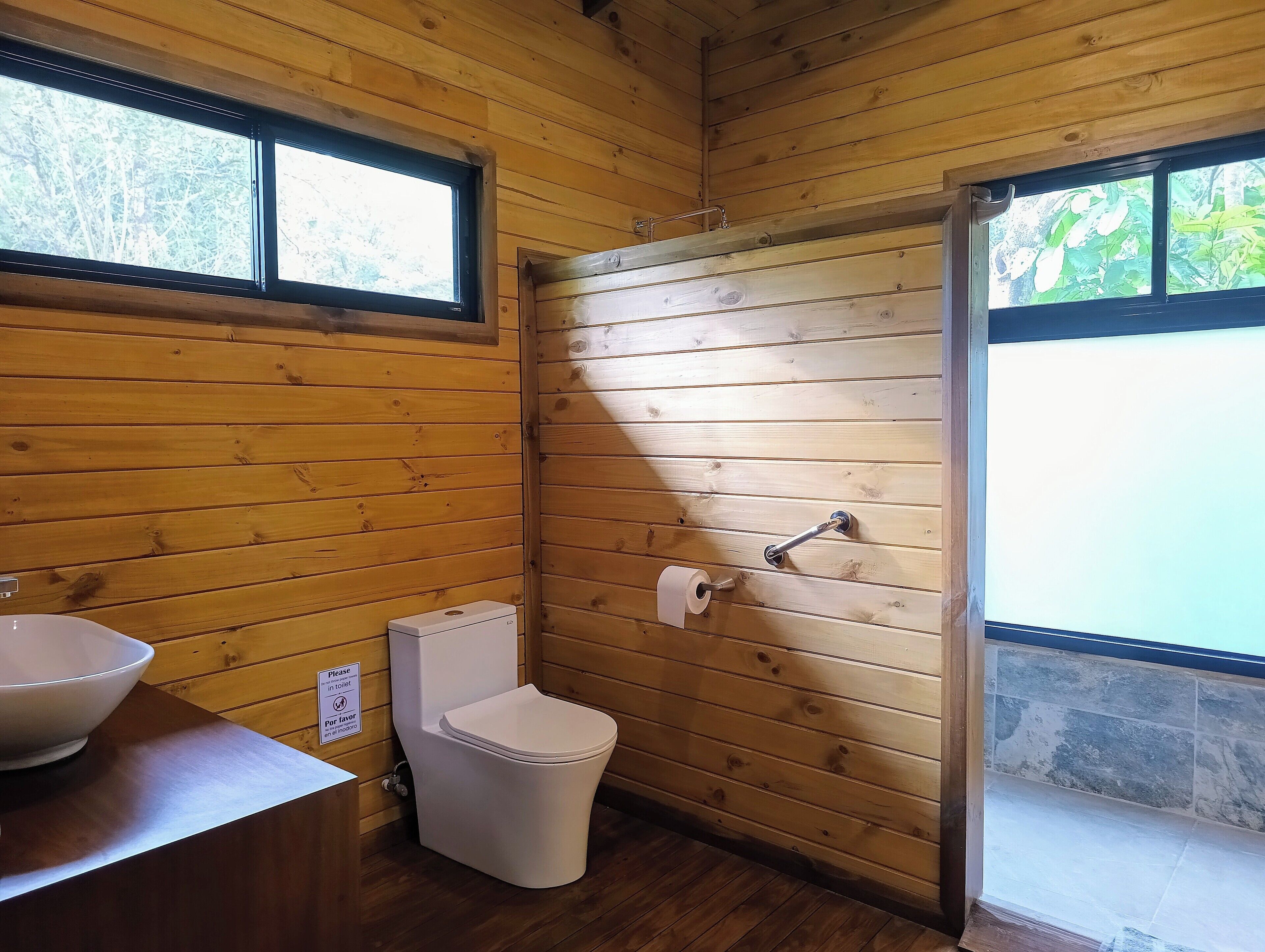 A wooden cabin bathroom with a toilet, sink, and shower.