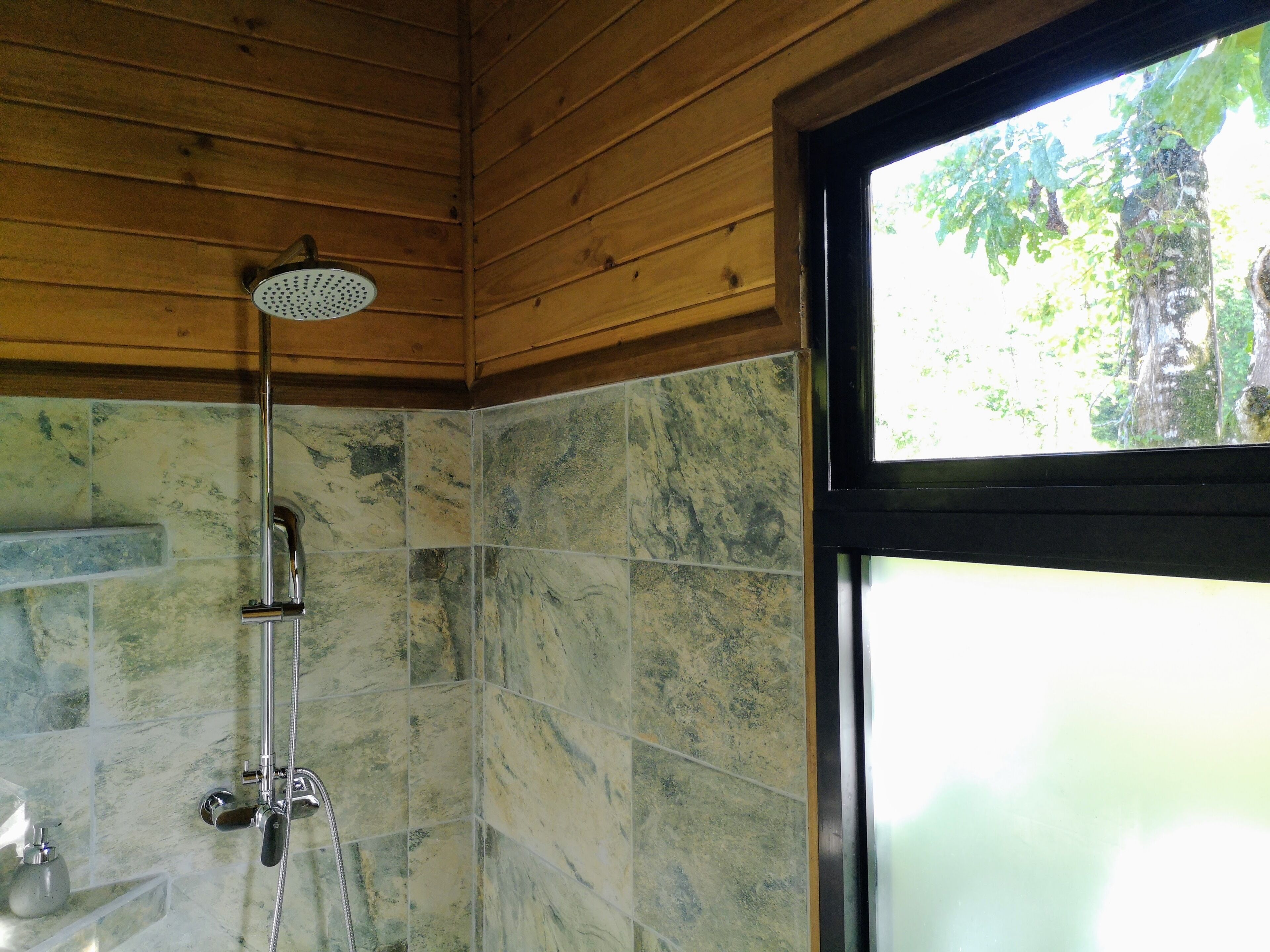 Un baño con ducha, paredes de azulejos y una ventana.