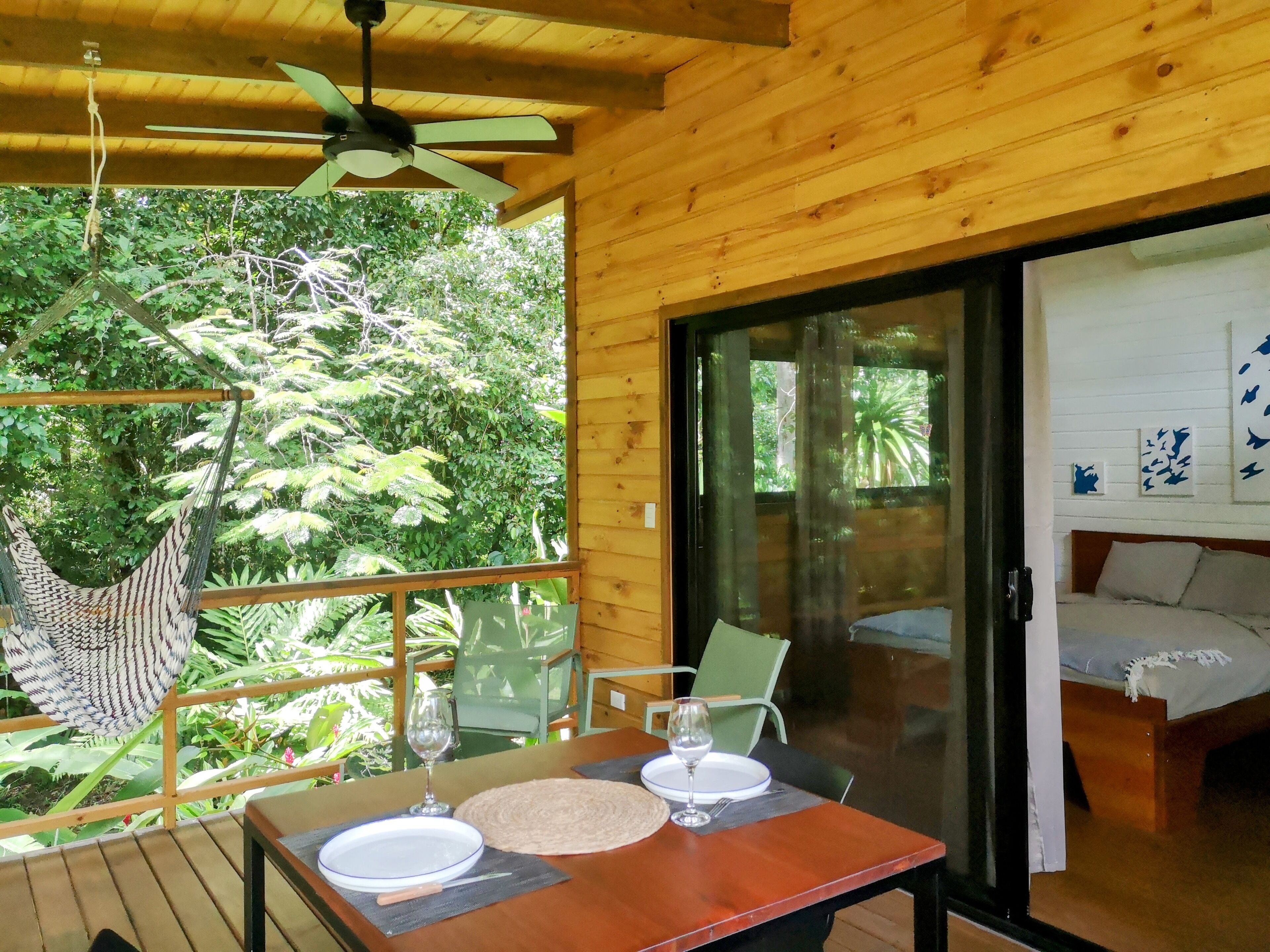 A wooden room with a bed, a table with a glass, and a hammock.