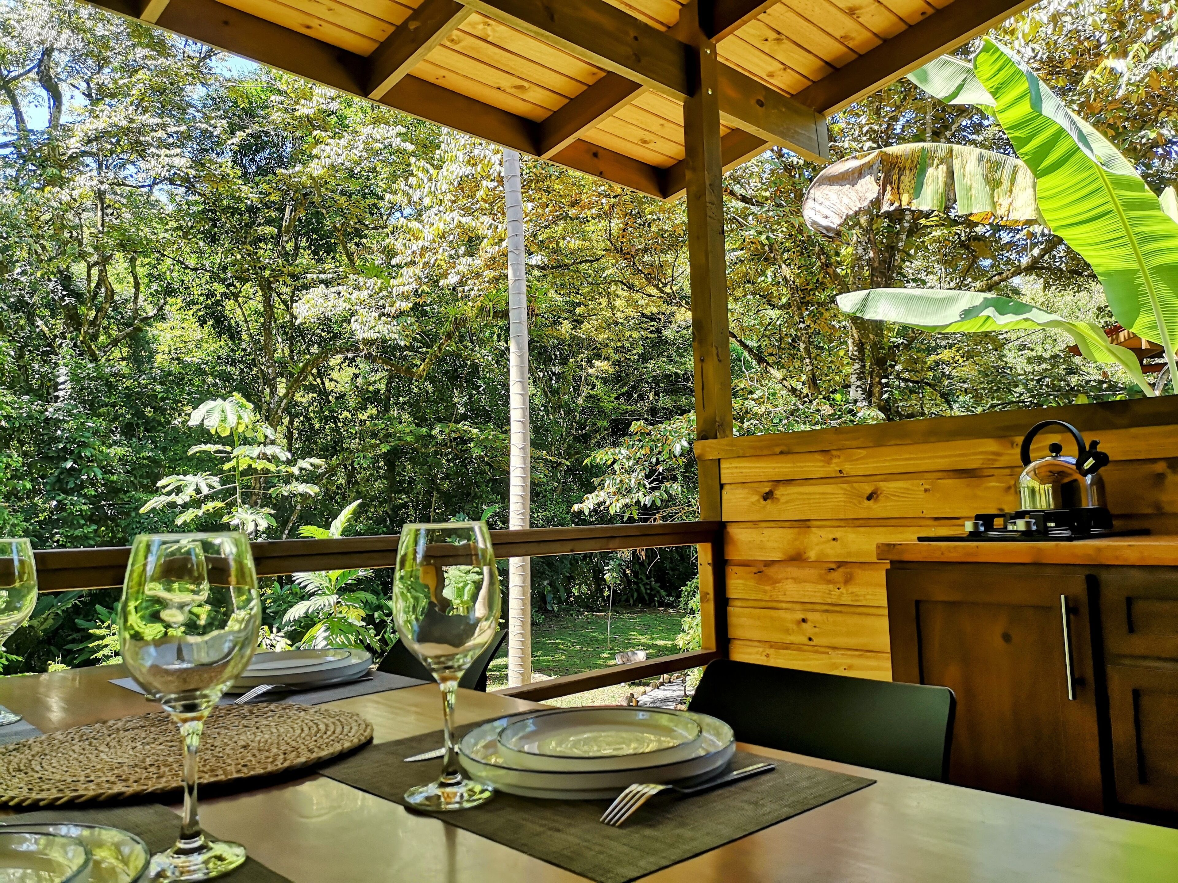 An outdoor dining area with wooden tables, chairs, and a view of lush greenery.