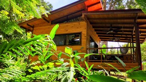 A wooden house with a porch, surrounded by lush greenery. - Thoas Lodge  (Ciudad Cortés)