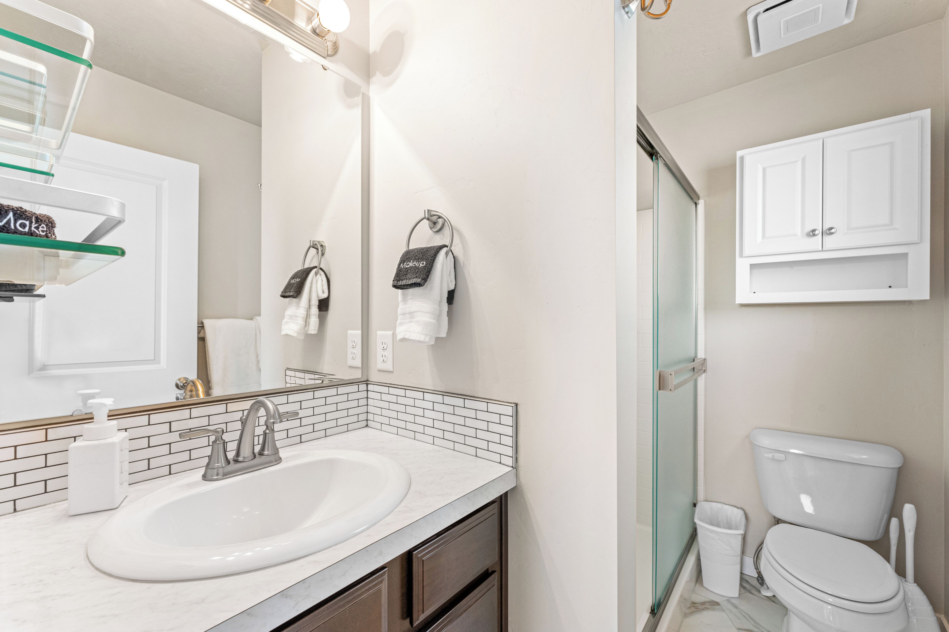 A modern bathroom with a white sink, a glass shower enclosure, and a white toilet.