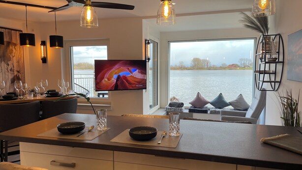 Eine moderne Küche mit einer großen Kochinsel, Esstischen und Sesseln, sowie einem Fernseher, der eine schöne Aussicht zeigt.