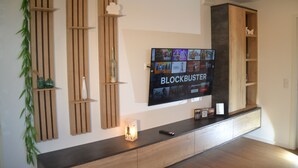 A modern living room with a mounted TV displaying 'BLOCKBUSTER' and a wooden entertainment unit with shelves. - * * * * * * Penthouse Meeresleuchten Duhner Entrée 19 (Cuxhaven)