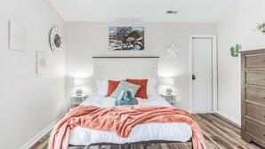 A bedroom with a bed, white headboard, two bedside tables with lamps, a star decoration, and a door.