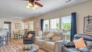 A spacious living room with a large window, a ceiling fan, and a dining area with a table and chairs.