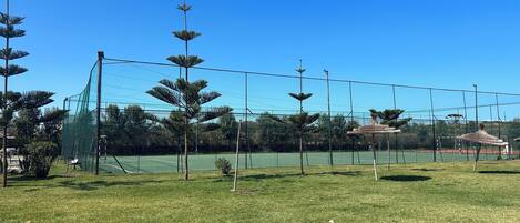 Una cancha de tenis con una red, rodeada por una valla y árboles.