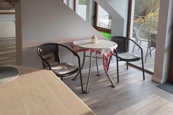A dining area with a table and two chairs, a view of the outdoors, and a staircase.
