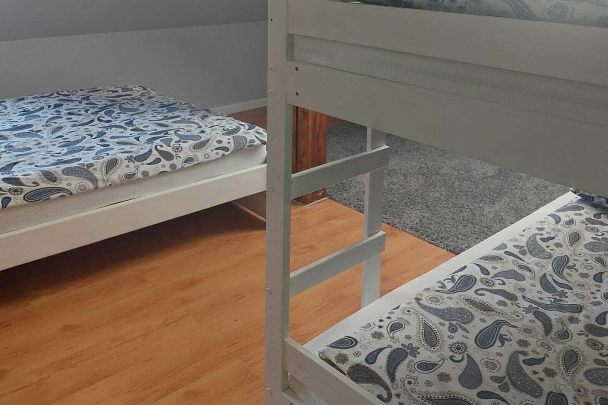 A bunk bed with patterned bedding, wooden flooring, and a grey carpet.