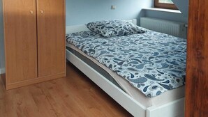 A bedroom with a wooden wardrobe, a bed with patterned bedding, and a white radiator. - Apartment in Sopot near Monte Cassino Street (Sopot)