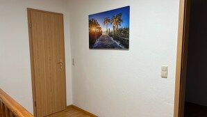 A hallway with a wooden door, a wooden staircase, and a wall-mounted picture of a beach scene. - Apartment in Zwickau Near Horch Museum (Zwickau)