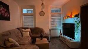 A cozy living room with a brown sofa, a small table, a fireplace, and a window with blinds. - Apartment in Zwickau Near Horch Museum (Zwickau)