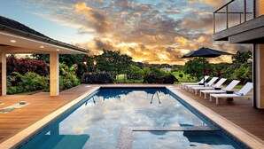 A rectangular pool with a wooden deck, lounge chairs, and umbrellas.