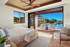 Un dormitorio con una cama grande, ventilador de techo y vistas a una piscina y zona de estar exterior.