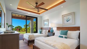 A modern bedroom with two beds, a ceiling fan, and a view of the outdoors.