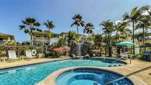 A pool area with a hot tub, lounge chairs, and palm trees.