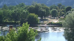 Un parc au bord de la rivière, avec des arbres, un petit pont et un bâtiment situé au loin.