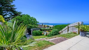 Jardim residencial com um caminho que leva a uma cerca de madeira com vista para uma praia.