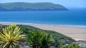 Paisagem costeira com uma praia, casas e uma colina ao fundo.