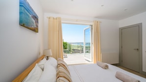 Quarto com uma cama grande, um quadro na parede e vista para o exterior através de uma porta de vidro.