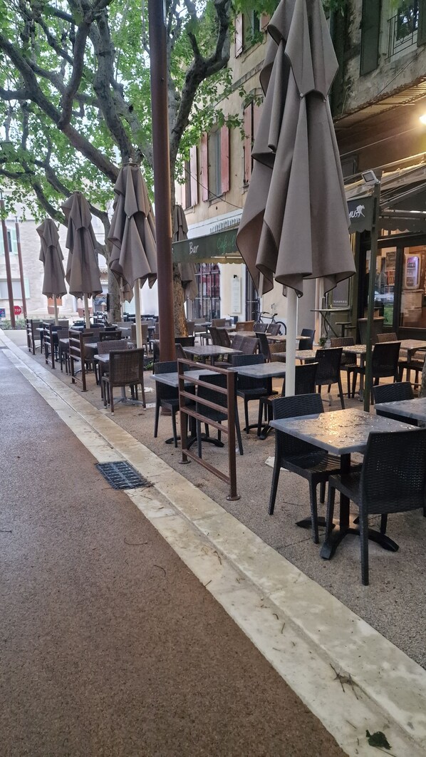 Outdoor seating with umbrellas, tables, and chairs, with a building in the background.