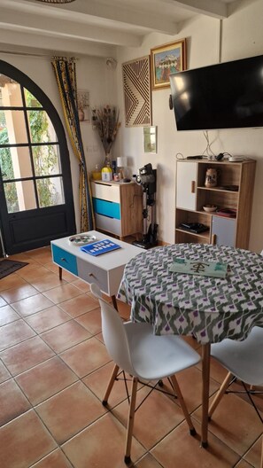 A dining area with a table and chairs, a television mounted on the wall, and a window with curtains.