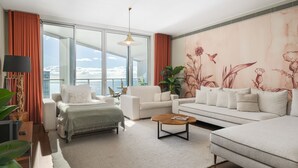A modern living room with a sofa, armchairs, a coffee table, and a large window offering a view of the sea. - Luxury apt in clifftop condo | Palace Ocean View (Funchal)