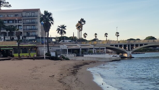 Une zone située au bord de la plage, avec un pont piétonnier enjambant l’eau, une plage de sable et des bâtiments dotés de balcons.