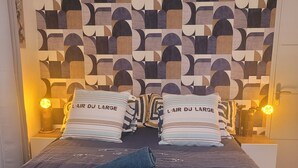 Un lit avec une tête de lit à motifs géométriques, des coussins ornés de motifs textuels et une serviette pliée.