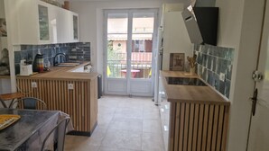 Une cuisine compacte dotée d’un plan de travail en bois, d’une table à manger et offrant une vue sur le balcon grâce à une porte vitrée.