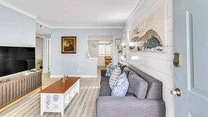 A modern living room with a sofa, a coffee table, a TV, and artwork on the walls. - Walk to Beach! Relaxing Villa w/ Pool Hilton Head (Hilton Head Island)