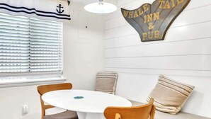 A room with a round table, two wooden chairs, a bench with cushions, a wall-mounted sign reading 'Whale Tail Inn & Pub', and a window with blinds. - Walk to Beach! Relaxing Villa w/ Pool Hilton Head (Hilton Head Island)