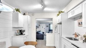 A modern kitchen with white cabinetry, a dining area with a wooden table, and a view into a living room. - Walk to Beach! Relaxing Villa w/ Pool Hilton Head (Hilton Head Island)